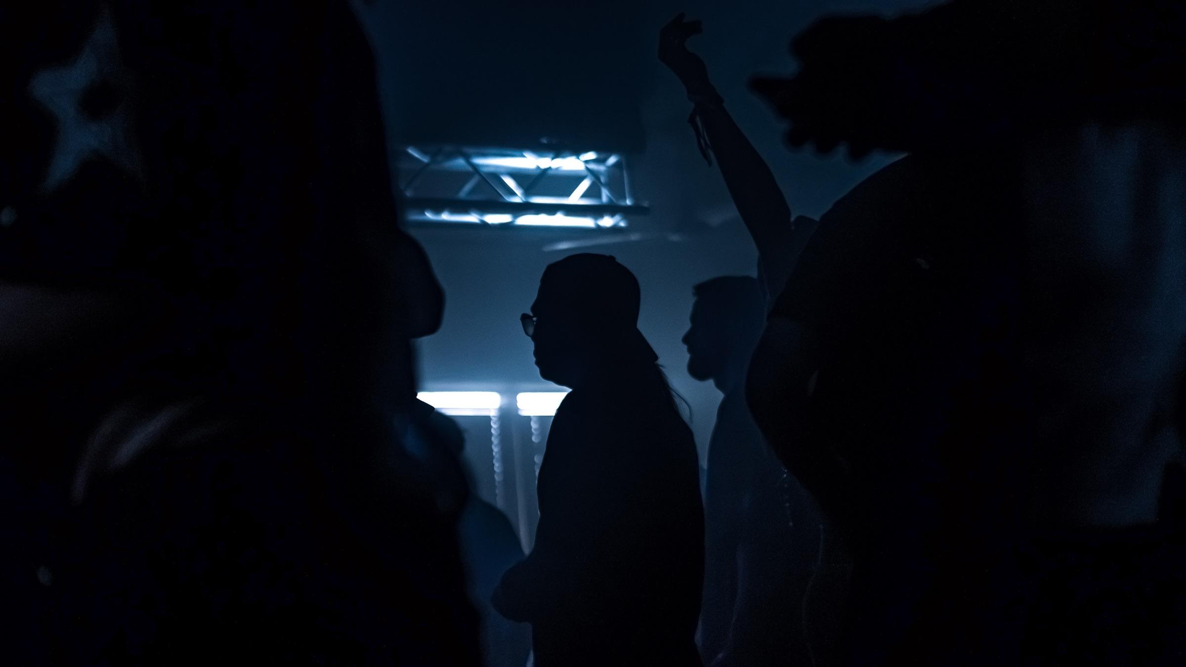 Crowd silhouettes under blue truss lights, one arm raised