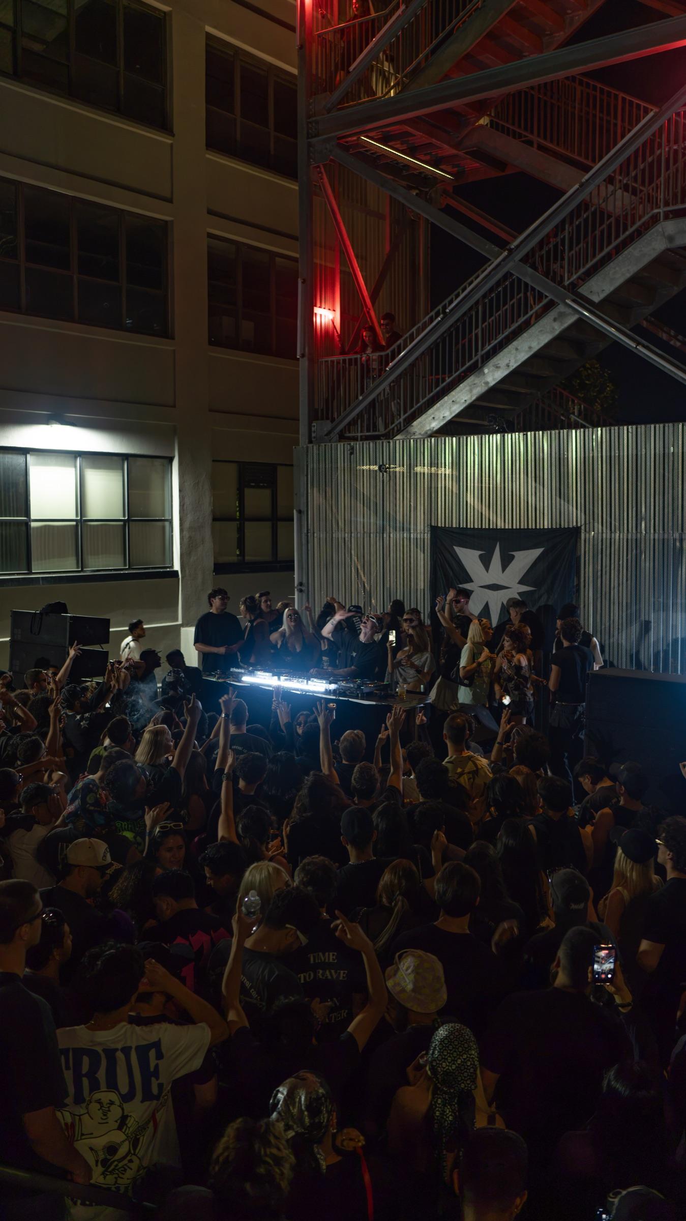 Crowd under red light and a steel fire escape