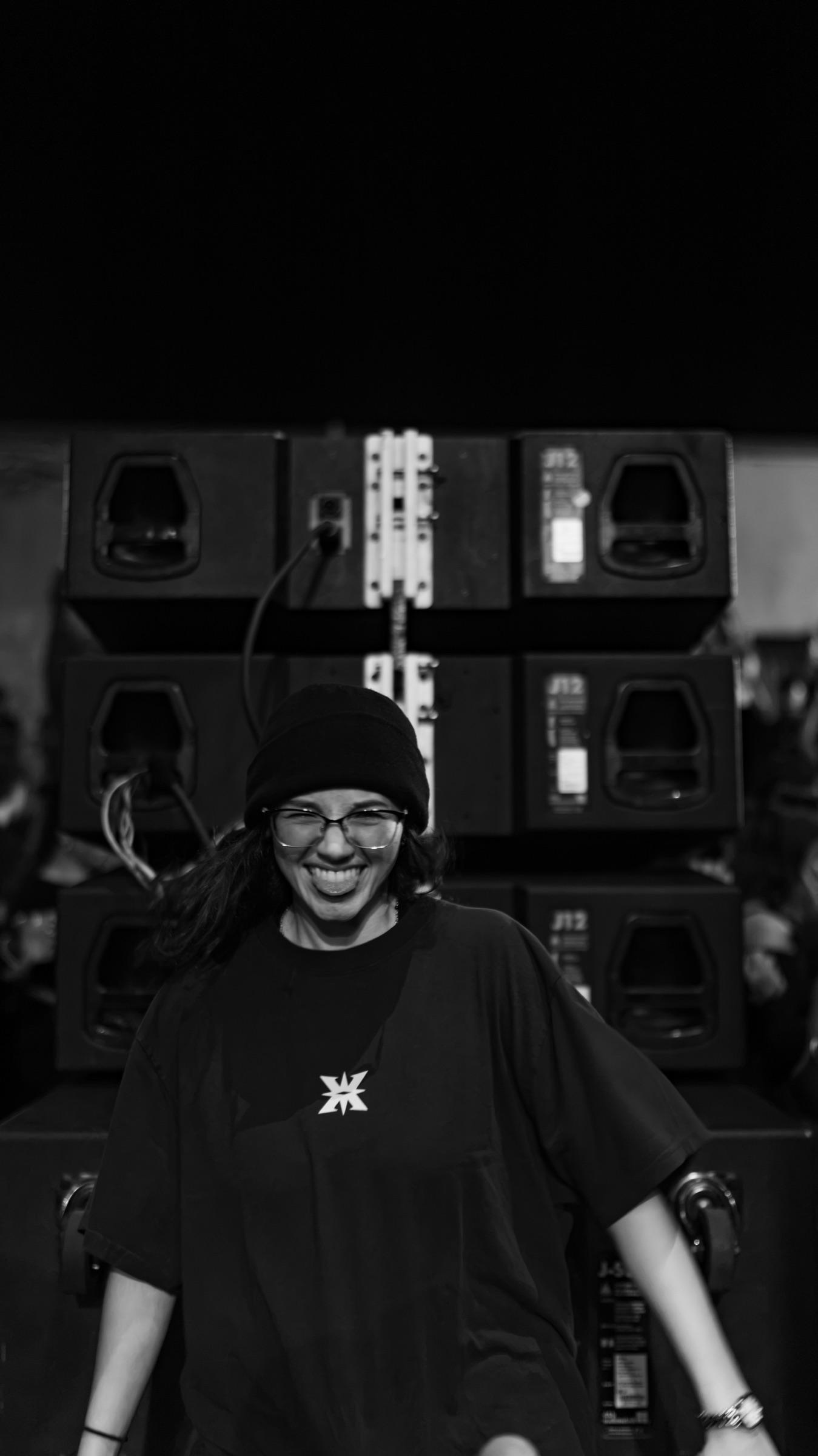 Black-and-white portrait of an artist smiling in front of a speaker stack