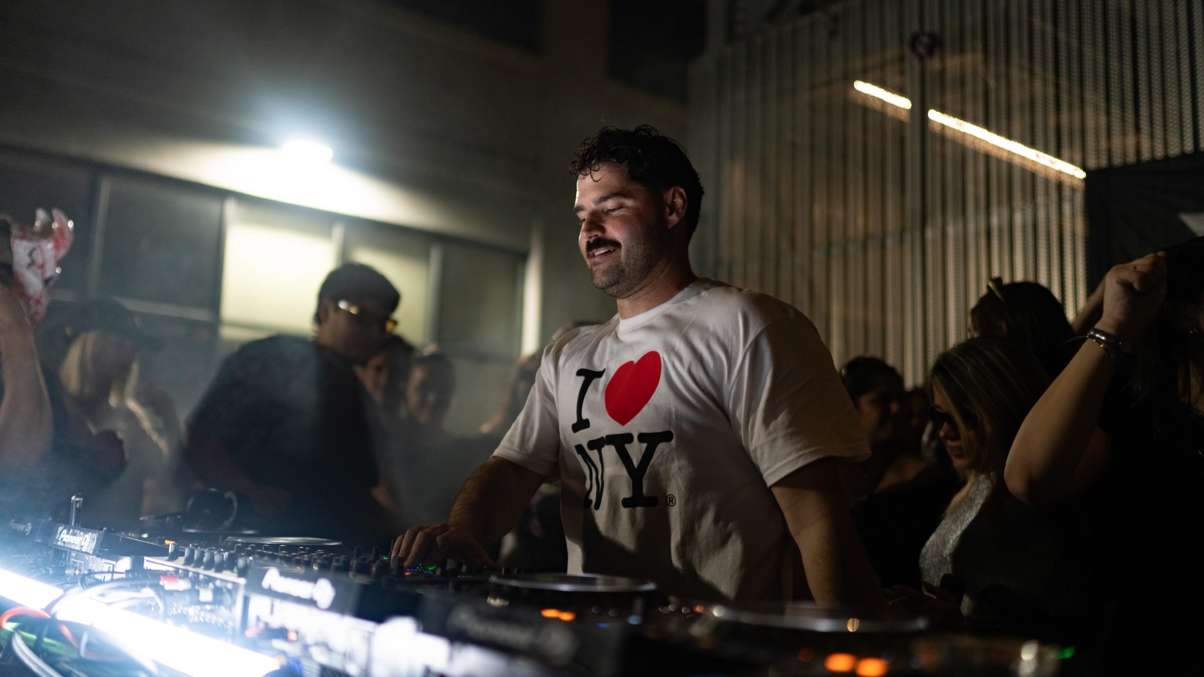 DJ in an I love NY shirt lit by an LED bar at the decks