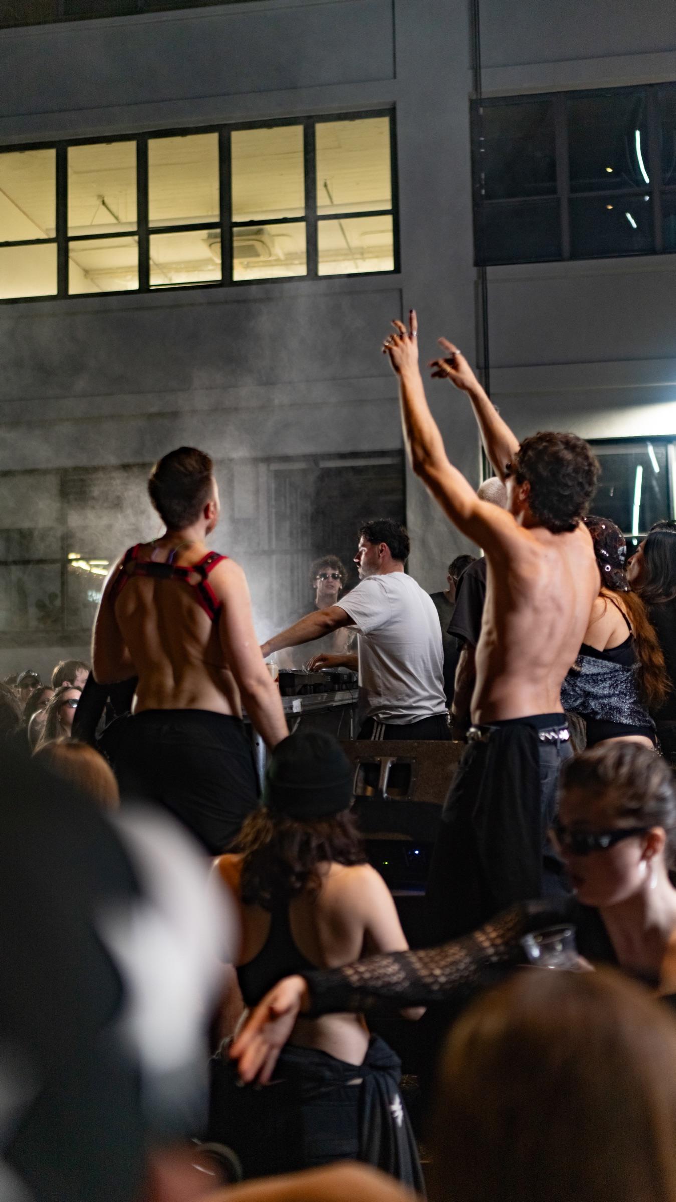 Shirtless dancers with arms up under lit windows
