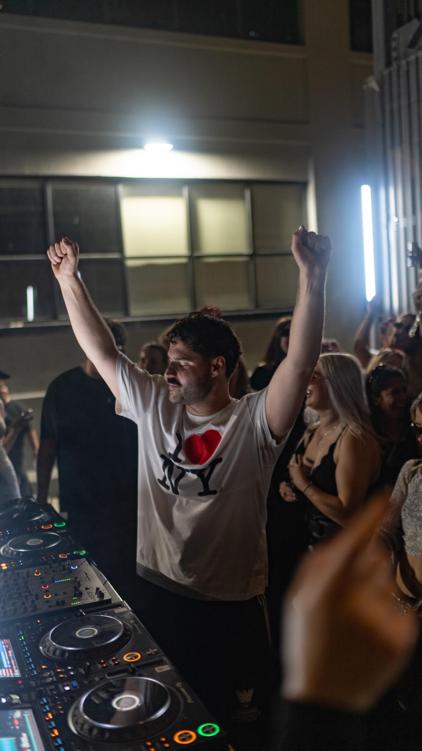 DJ with both arms up behind the decks