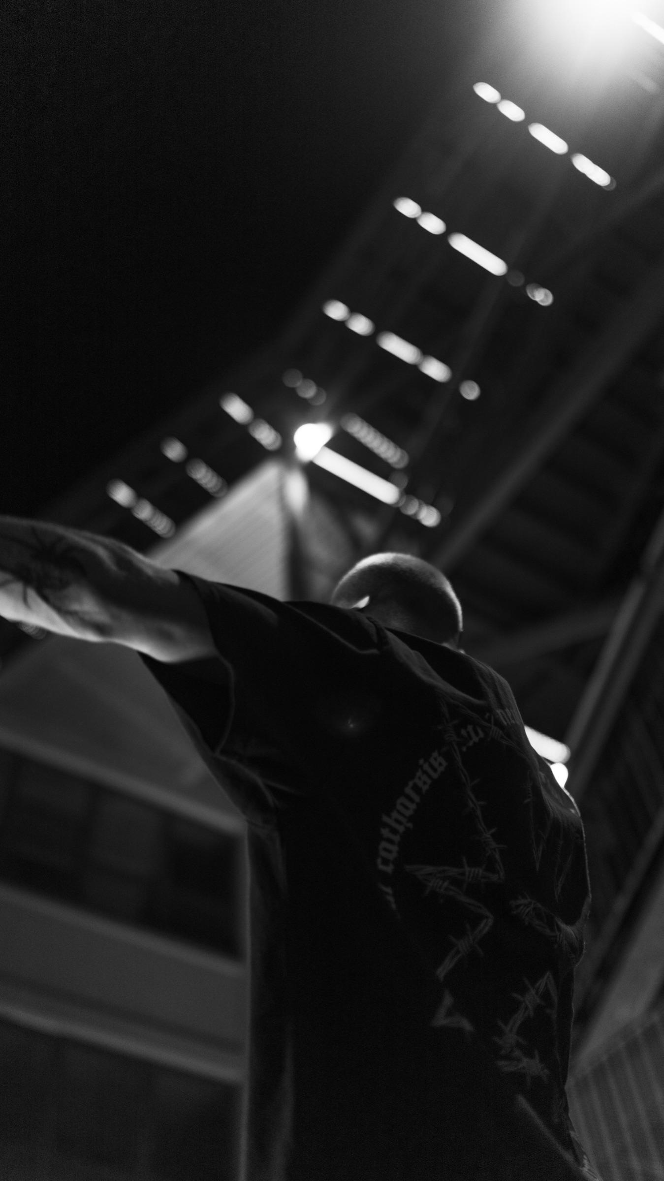 Black-and-white silhouette with arms out under stairwell lights