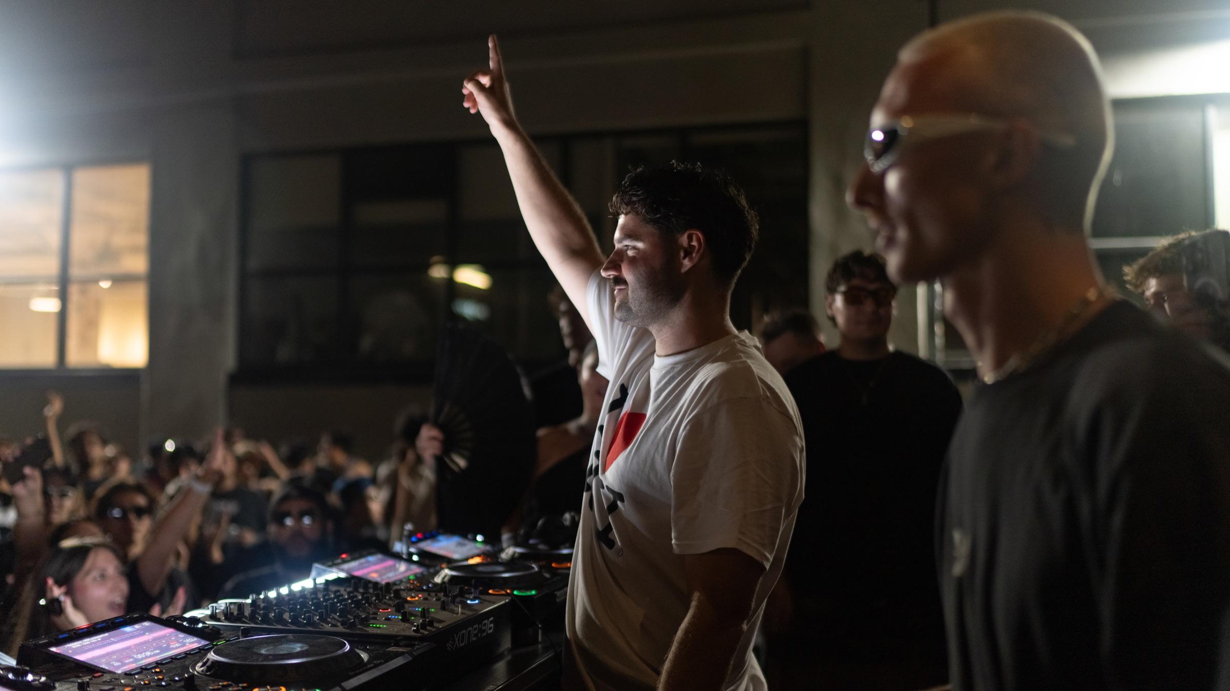Two DJs at the booth, one with an arm raised