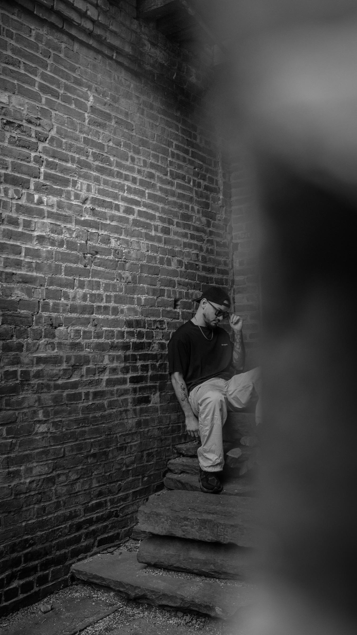 Medina seated on stone steps between brick walls, vertical frame