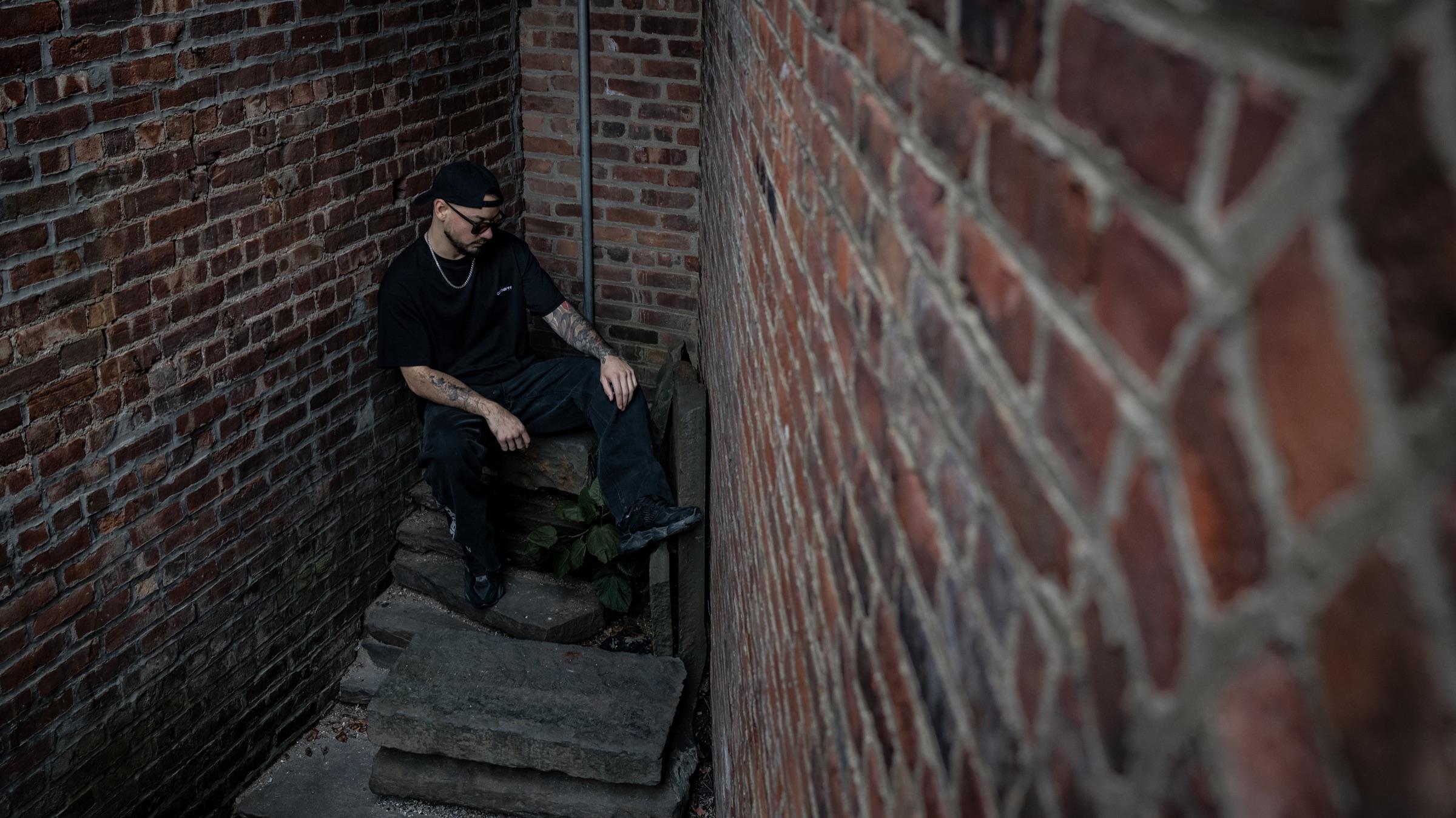 Medina seated in the alley, brick wall angled across the frame
