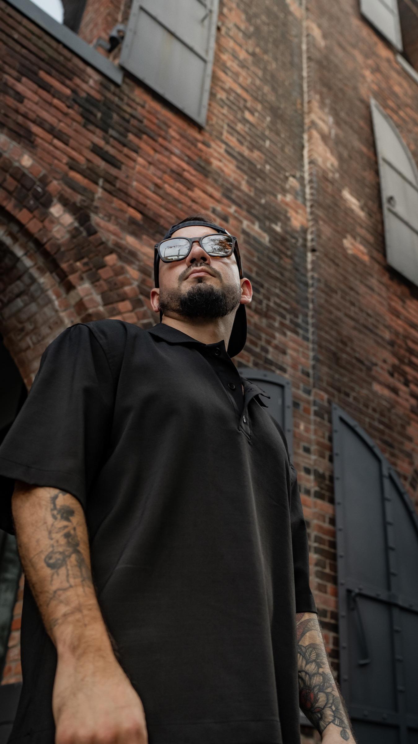 Low angle of Medina in glasses against a brick warehouse