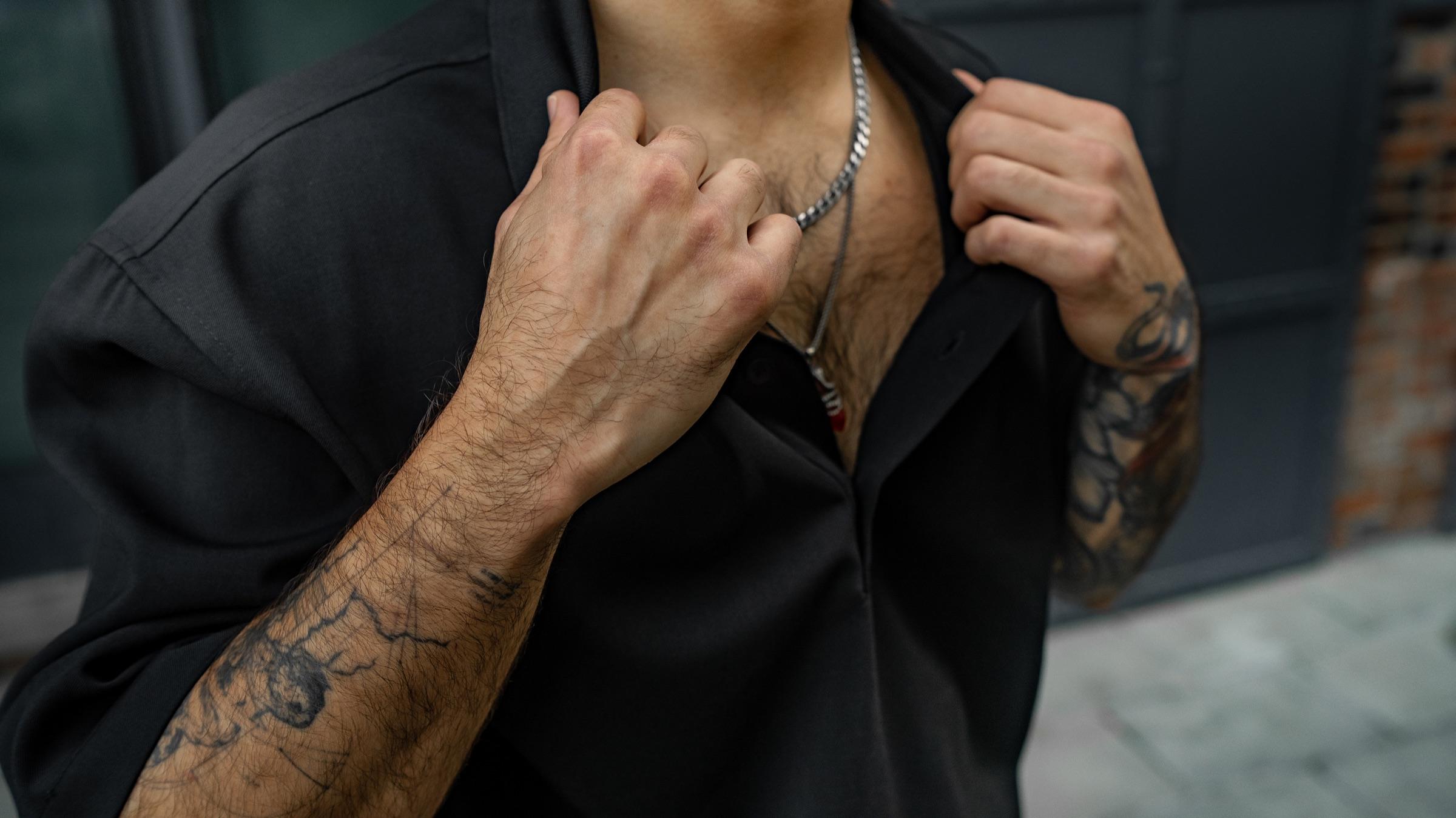 Close-up of tattooed hands at the collar of a black shirt