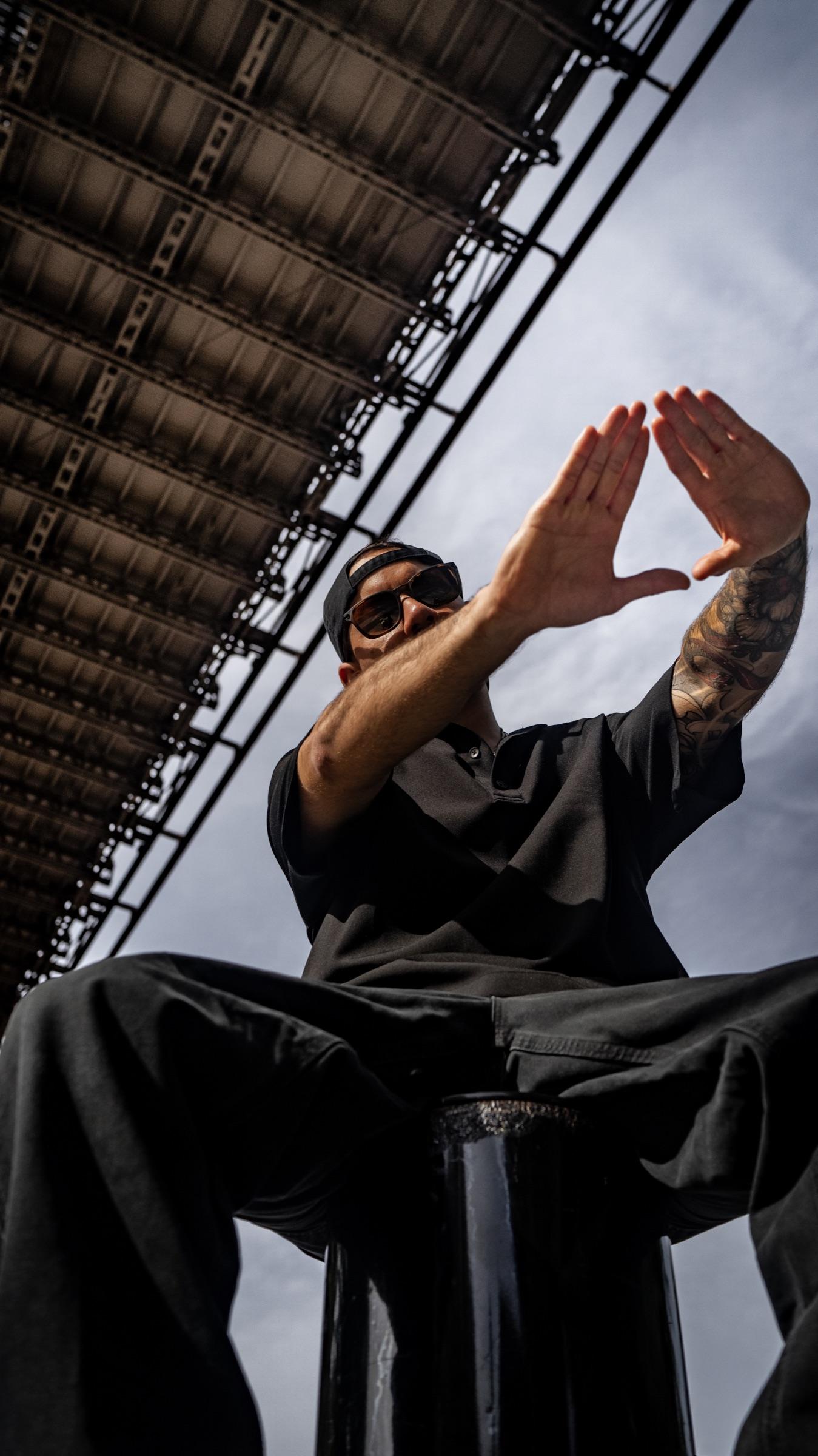 Medina seated under a steel walkway, hands forming a triangle
