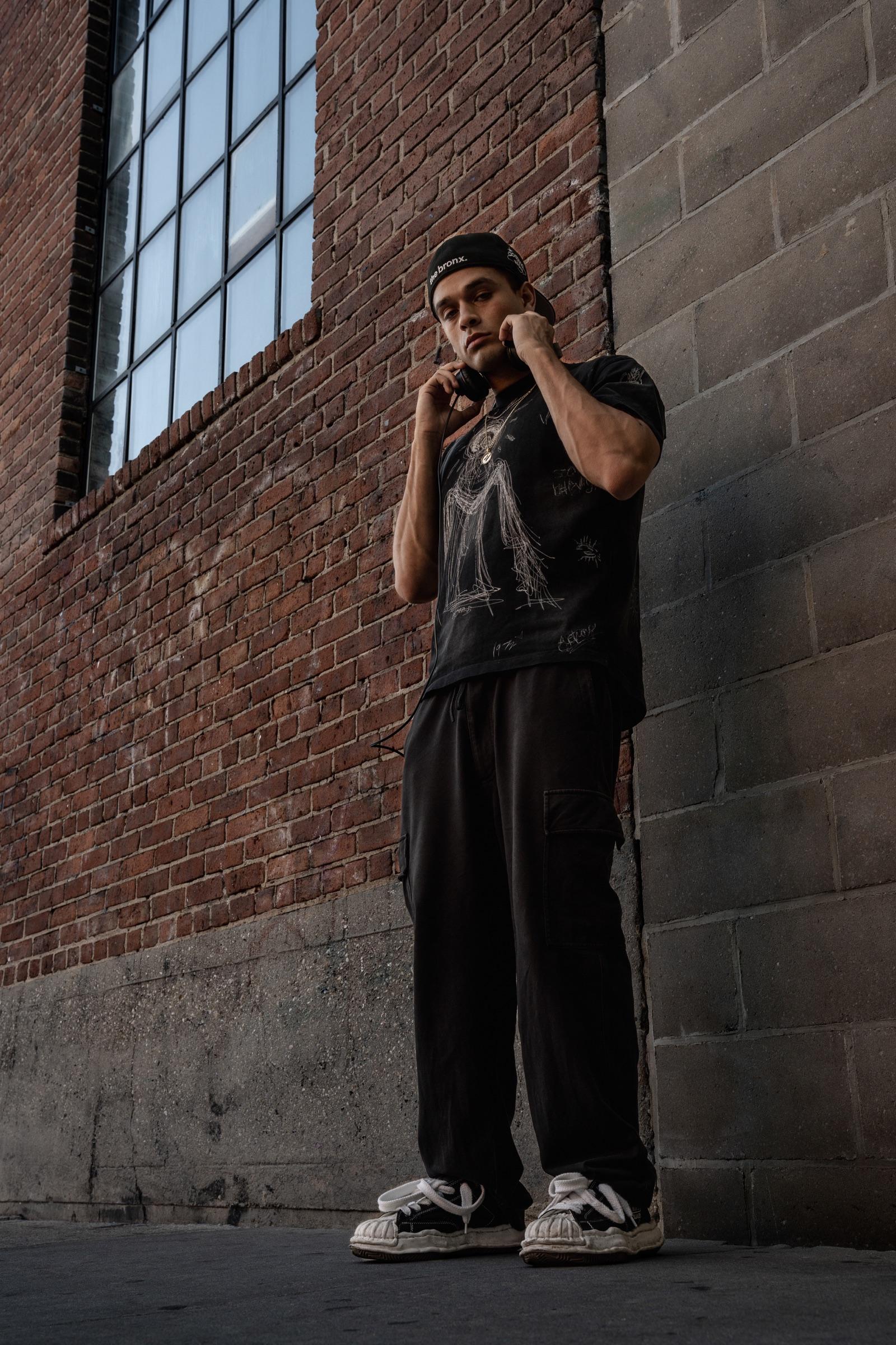 Artist standing against a brick wall, hands on headphones