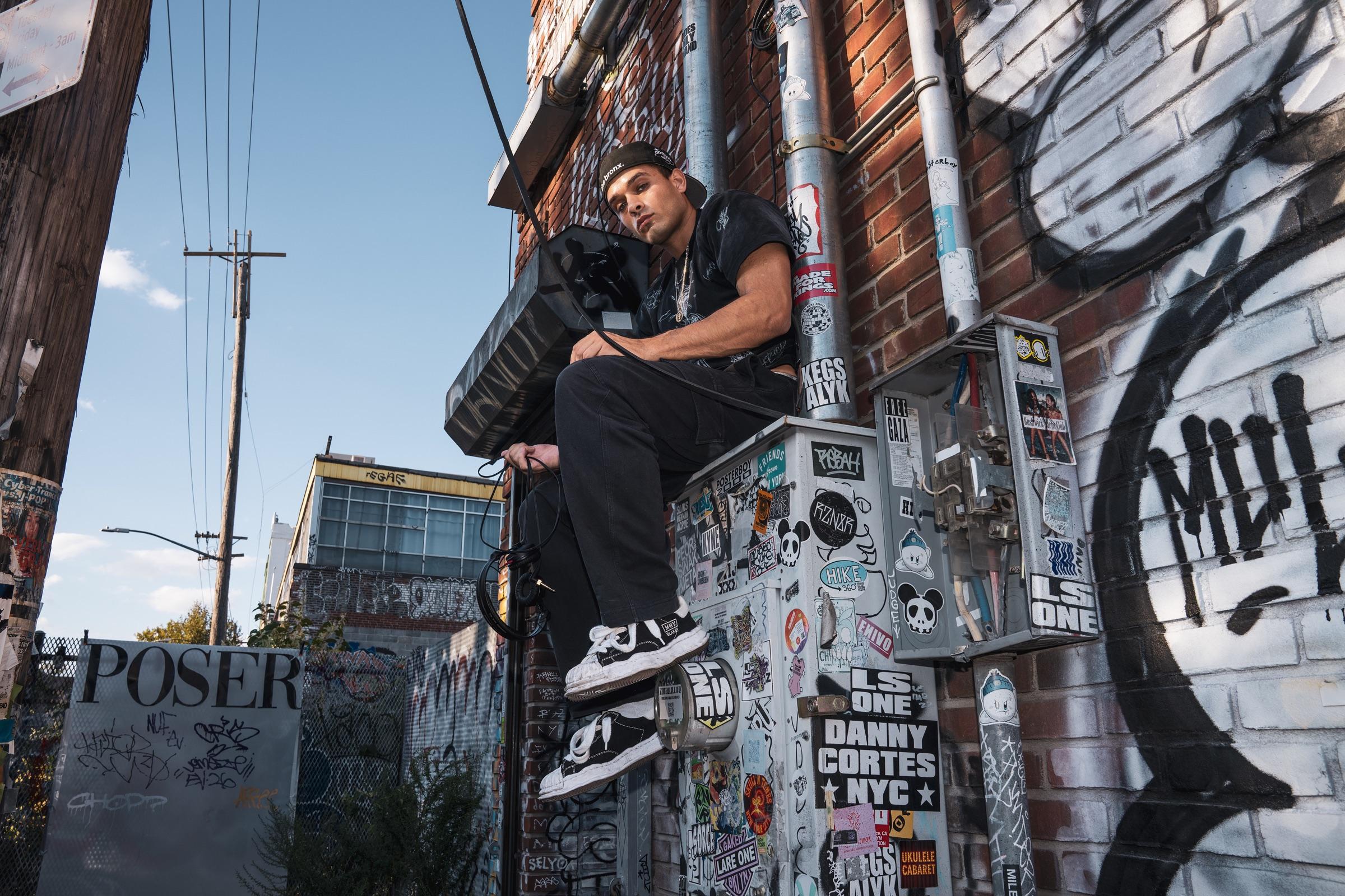 Artist sitting on a graffiti wall, utility poles behind