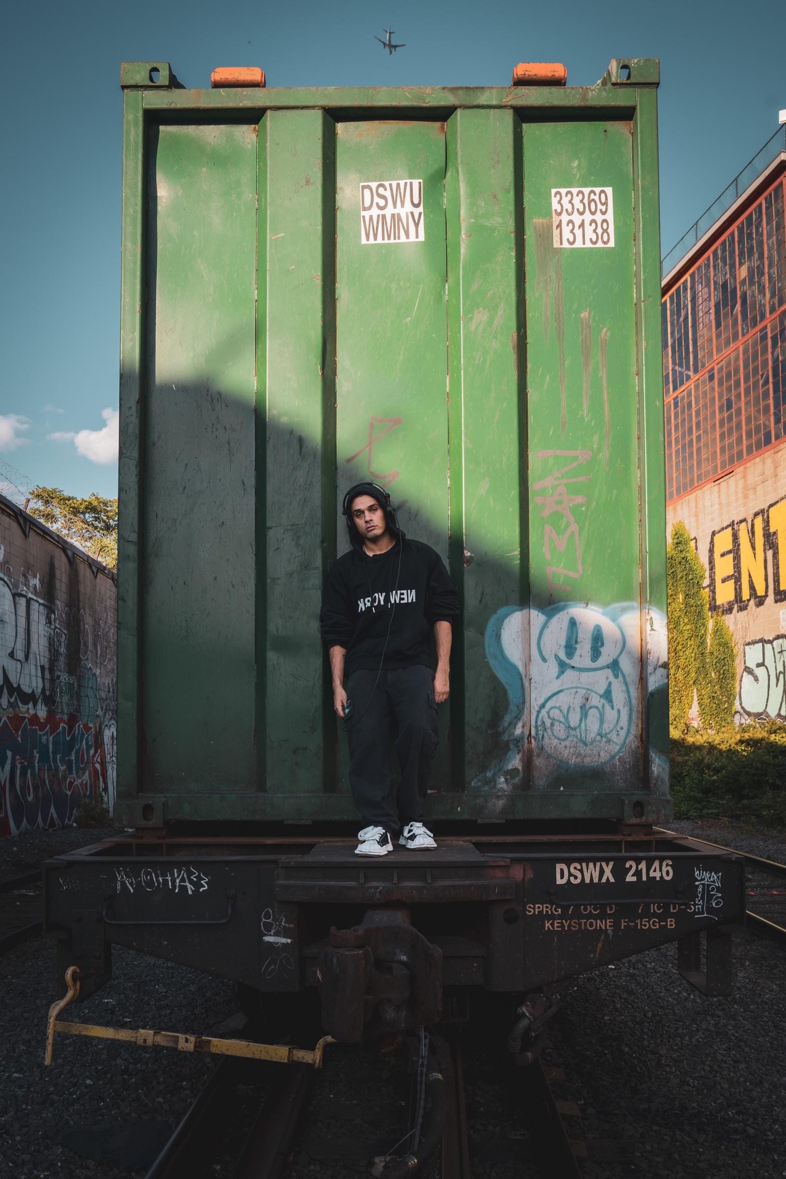 Artist standing small in front of a green container