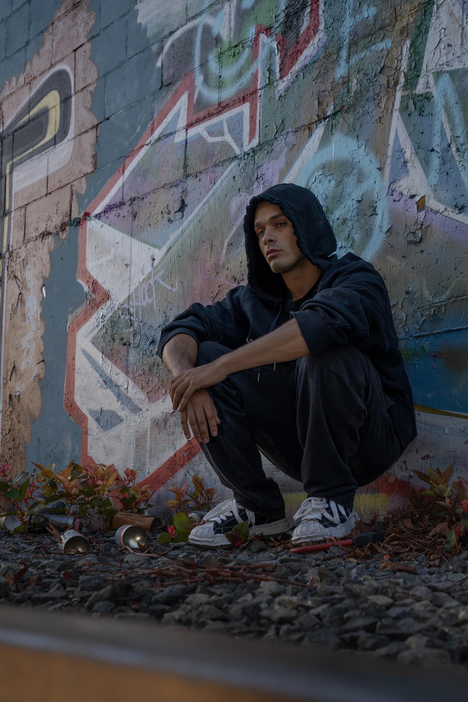Artist crouched in front of a graffiti mural