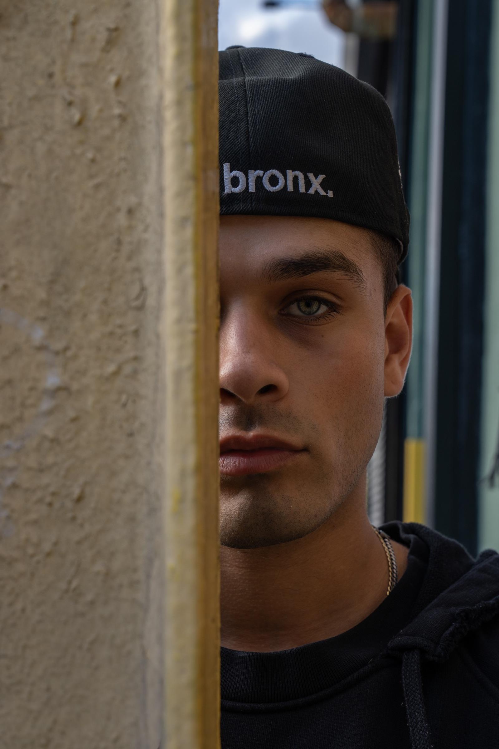 Close portrait half hidden behind a post, 'the bronx' cap