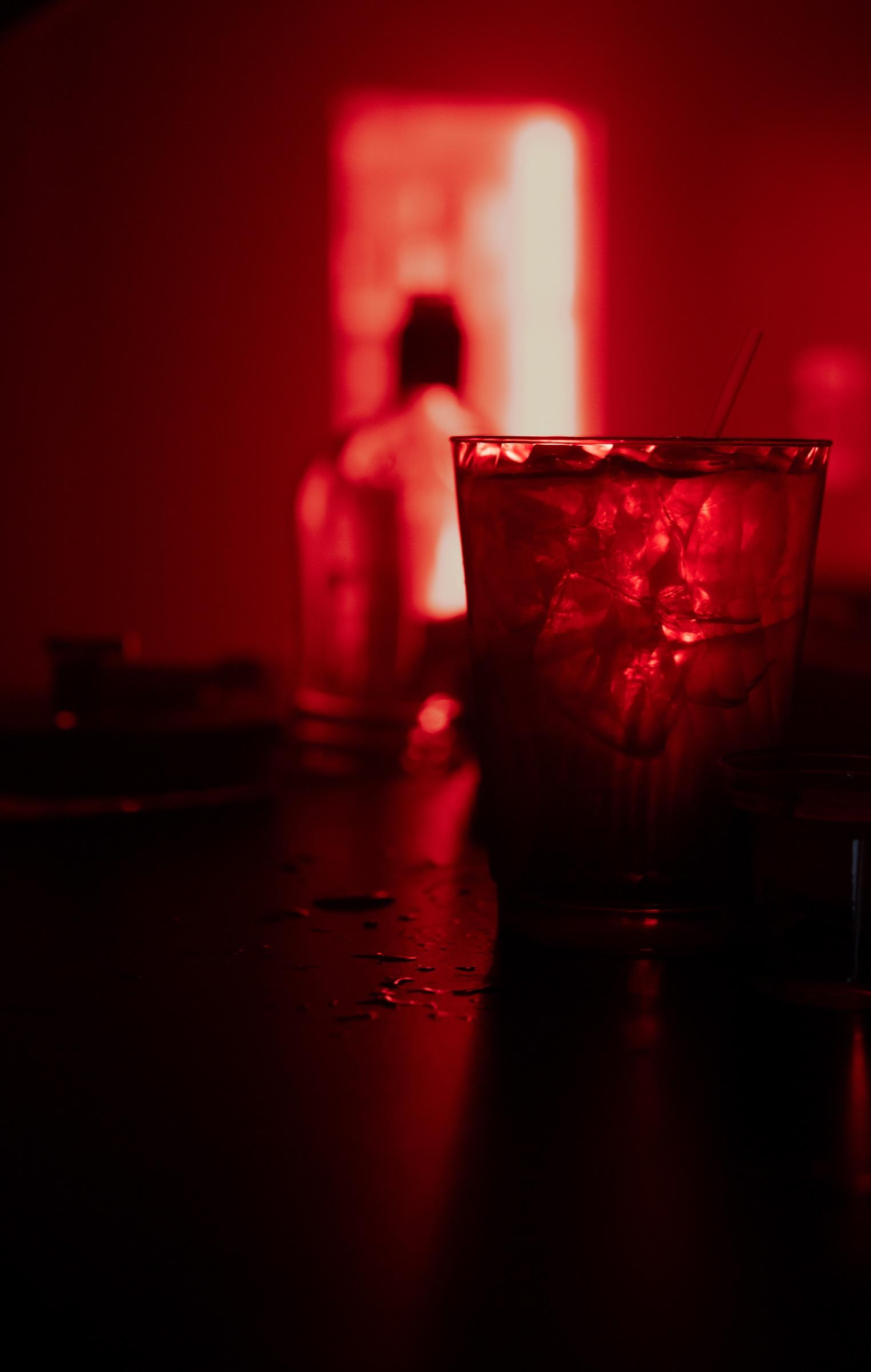 Glass on the bar glowing red, figure in a red doorway