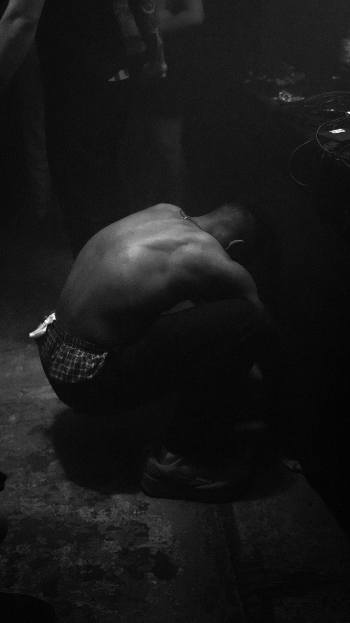Black-and-white: shirtless figure crouched, head down